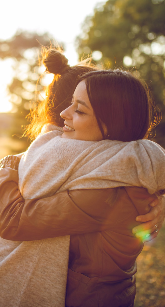 Two young caucasian beautiful women hugging in public park. Autumn time.