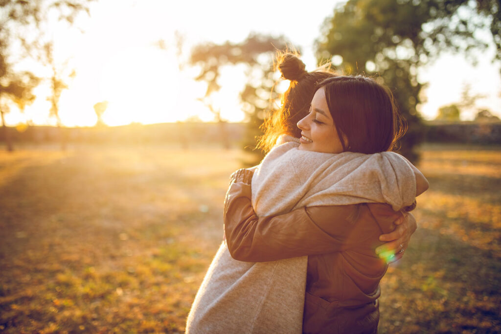 Two young caucasian beautiful women hugging in public park. Autumn time.