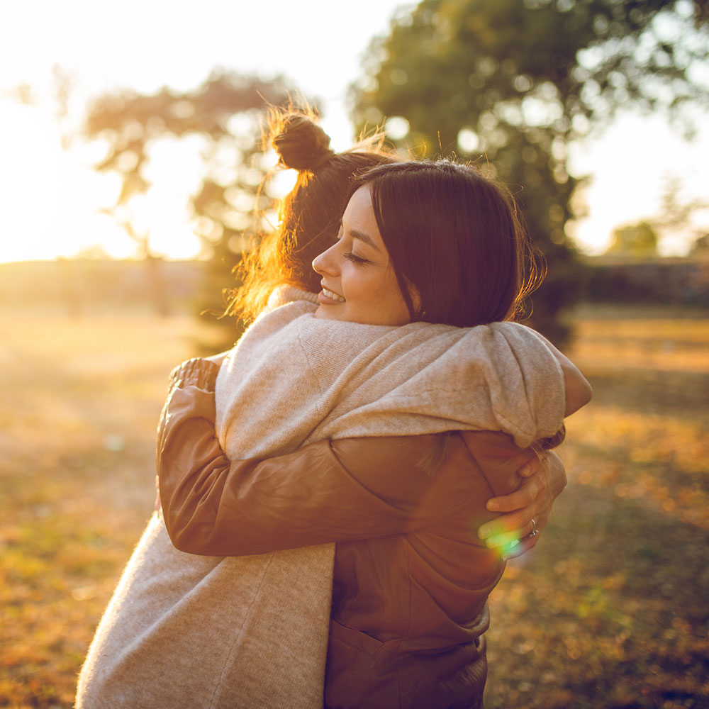 Two young caucasian beautiful women hugging in public park. Autumn time.